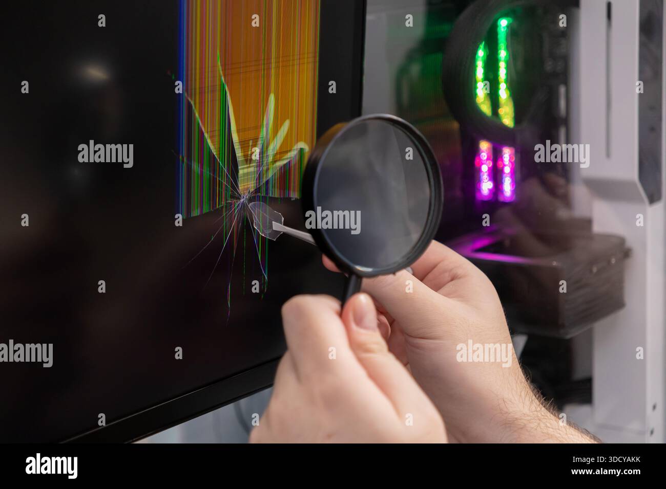Le mani umane utilizzano una lente d'ingrandimento per esaminare uno schermo rotto del computer con una lente d'ingrandimento rotta e colorate linee di glitch, raffiguranti un servizio IT urgente e. Foto Stock