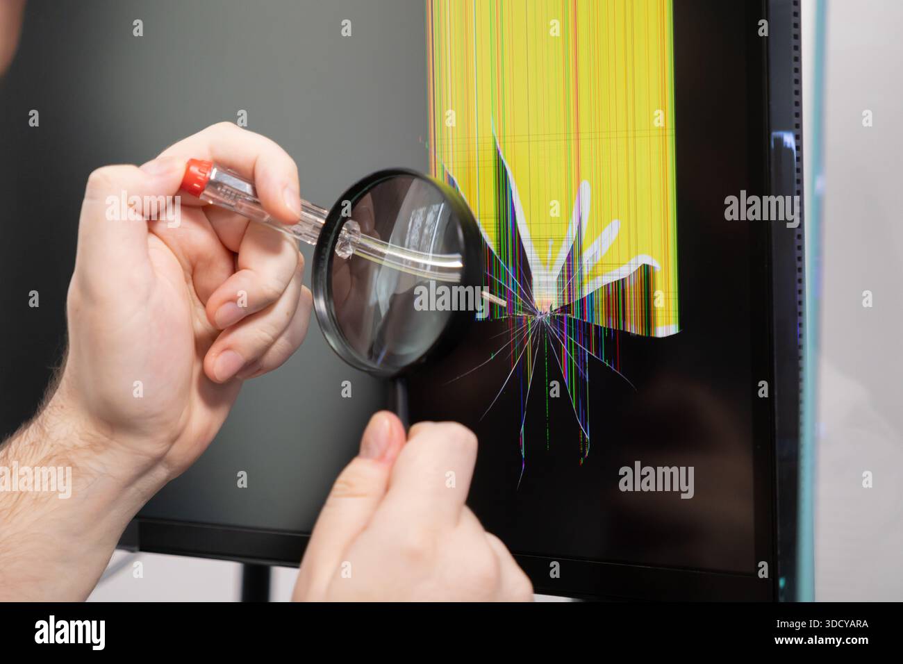Le mani con una lente d'ingrandimento esaminano uno schermo rotto del computer, visualizzando linee verticali gialle e danni ai pixel, essenziali per la risoluzione dei problemi elettronici Foto Stock