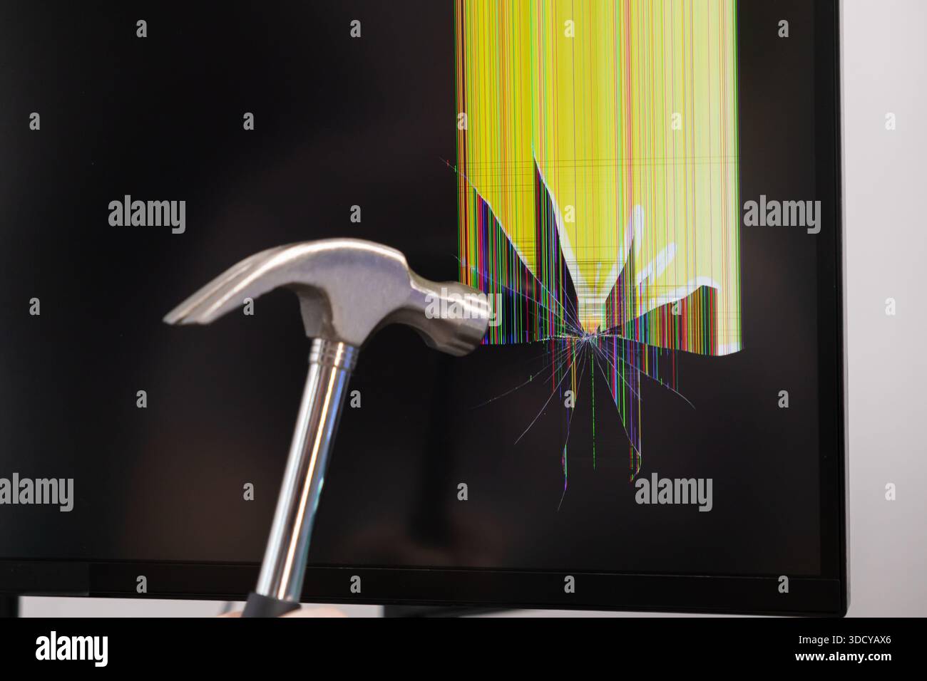 Vista ravvicinata di un potente martello metallico che ruota verso uno schermo rotto, visualizzando pixel colorati distorti verticalmente e crepe radiali, Foto Stock