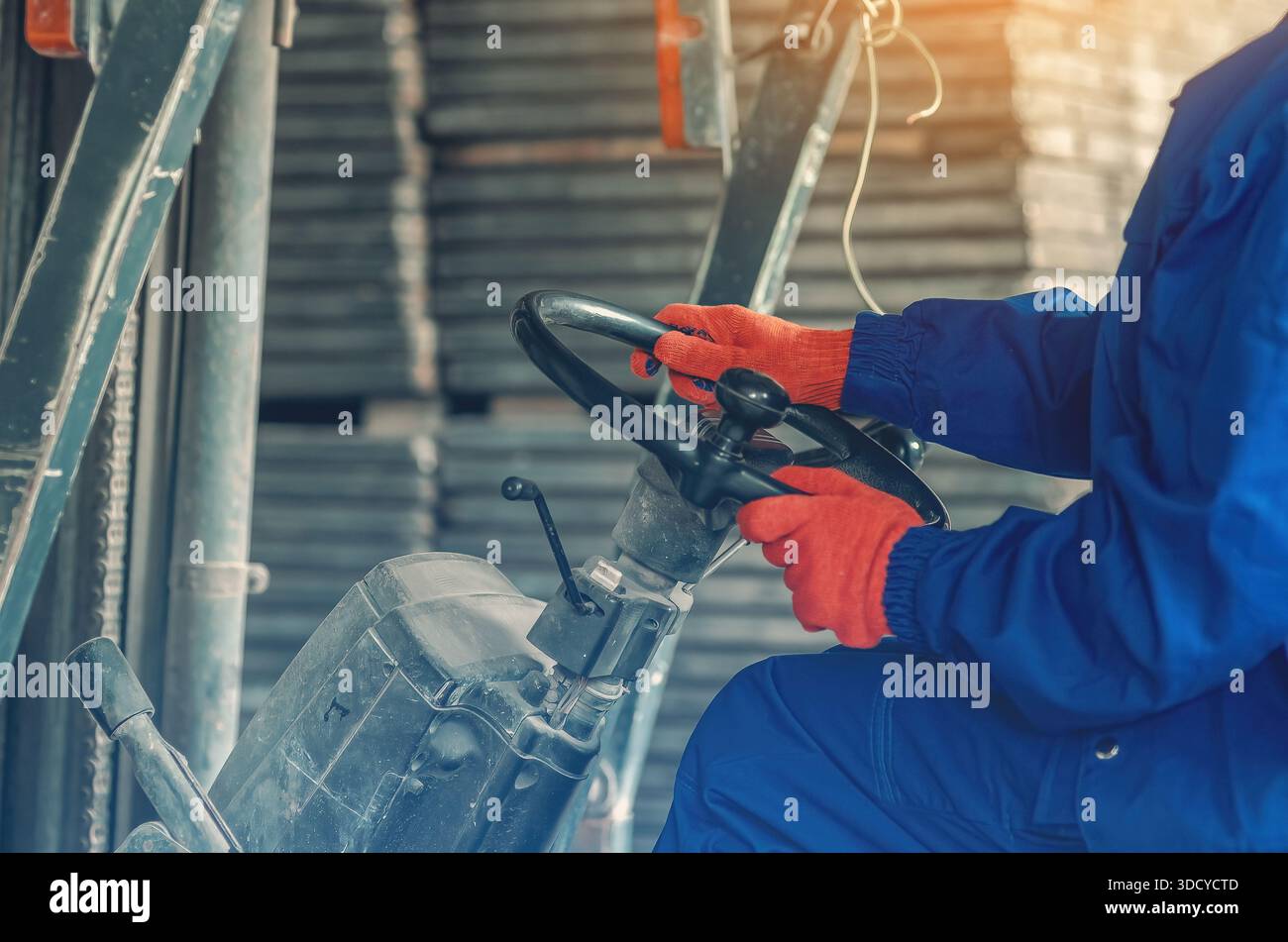 Donna in abbigliamento da lavoro blu che guida carrelli elevatori all'interno di un magazzino industriale. Lavoratore professionista che opera macchinari pesanti in ambito logistico o produttivo Foto Stock