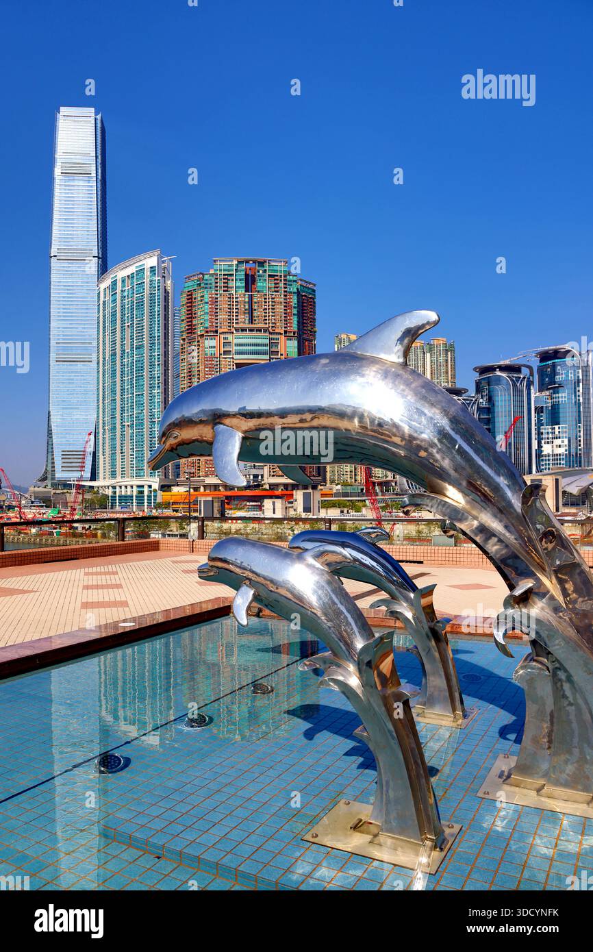 Statue di delfini al tramonto al Gateway Promenade di Tsim Sha Tsui con la Torre ICC e lo sviluppo di Union Square alle spalle, Hong Kong, Cina Foto Stock