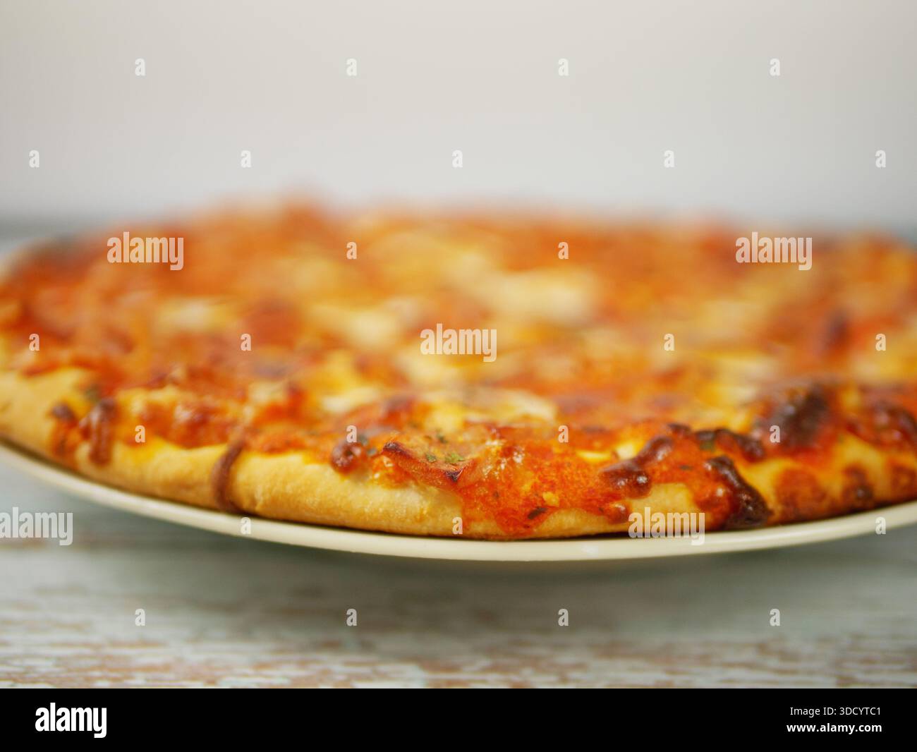 Pizza intera servita su piatto vista da Low Angle che enfatizza lo spessore della crosta e lo stile casalingo informale. Foto di alta qualità di Una pizza intera Foto Stock
