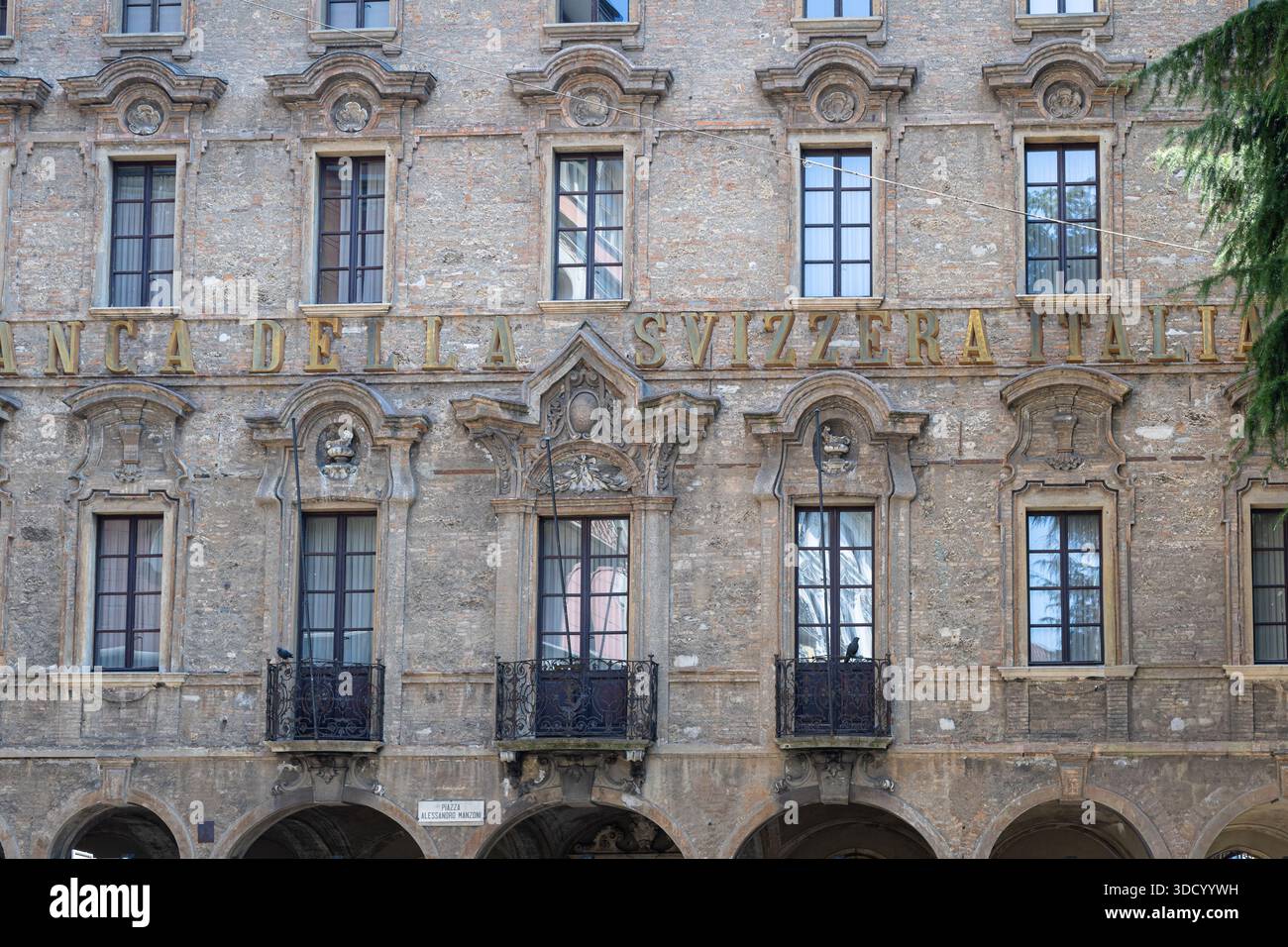 LUGANO, SVIZZERA, 06.20.2025: Una storica facciata italiana presenta pietre intemprate, frontoni decorativi e balconi in ferro battuto. Esterno illuminato dal sole Foto Stock