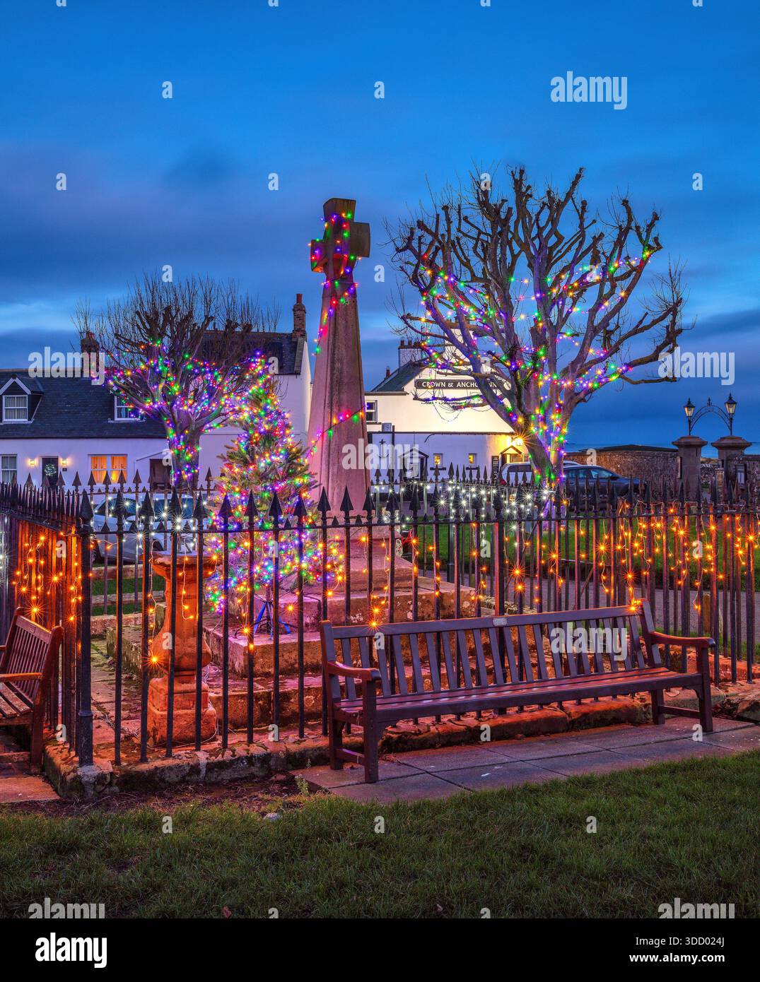 Una vista al crepuscolo di Natale dello spettacolo delle luci di Natale nella piazza del villaggio, memoriale di guerra sull'Isola Santa di Lindisfarne nel Northumberland Foto Stock
