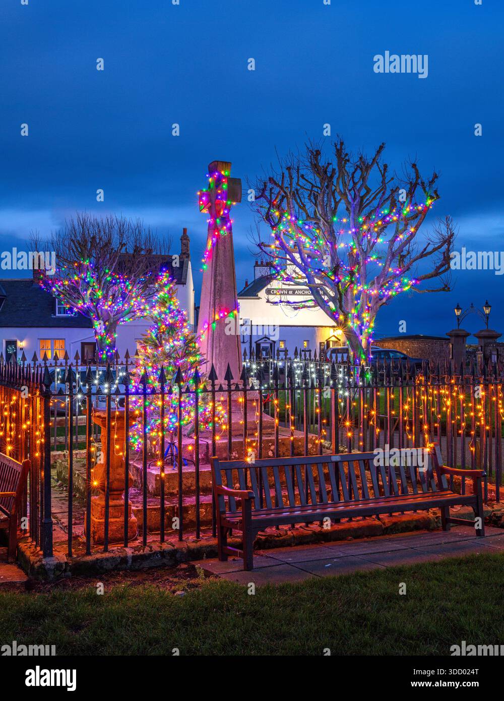 Una vista al crepuscolo di Natale dello spettacolo delle luci di Natale nella piazza del villaggio, memoriale di guerra sull'Isola Santa di Lindisfarne nel Northumberland Foto Stock