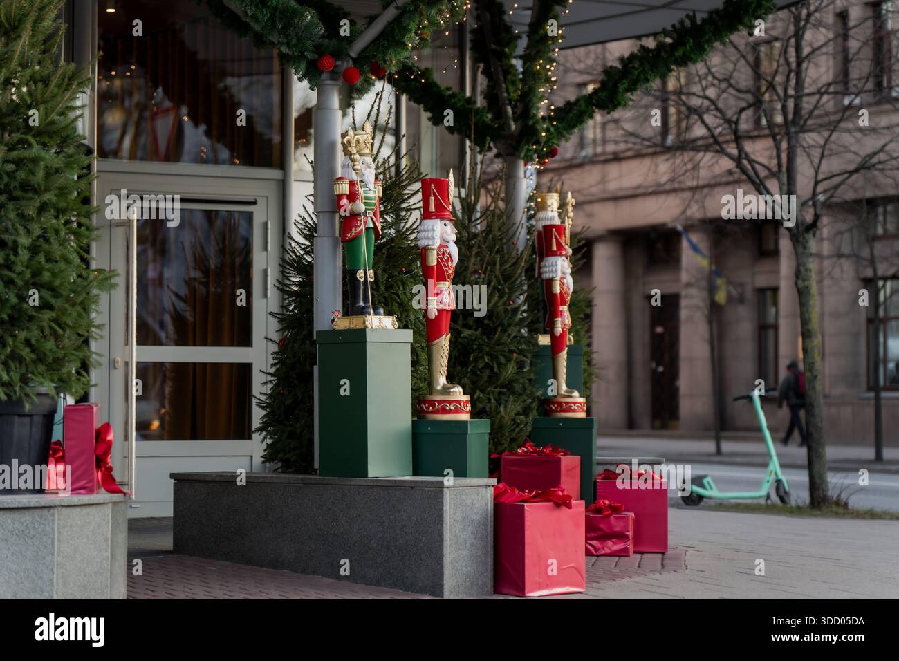 Scena di decorazione natalizia urbana a riga con figure dello schiaccianoci, vegetazione festosa e mostre di regali natalizi lungo l'architettura della strada della città Foto Stock