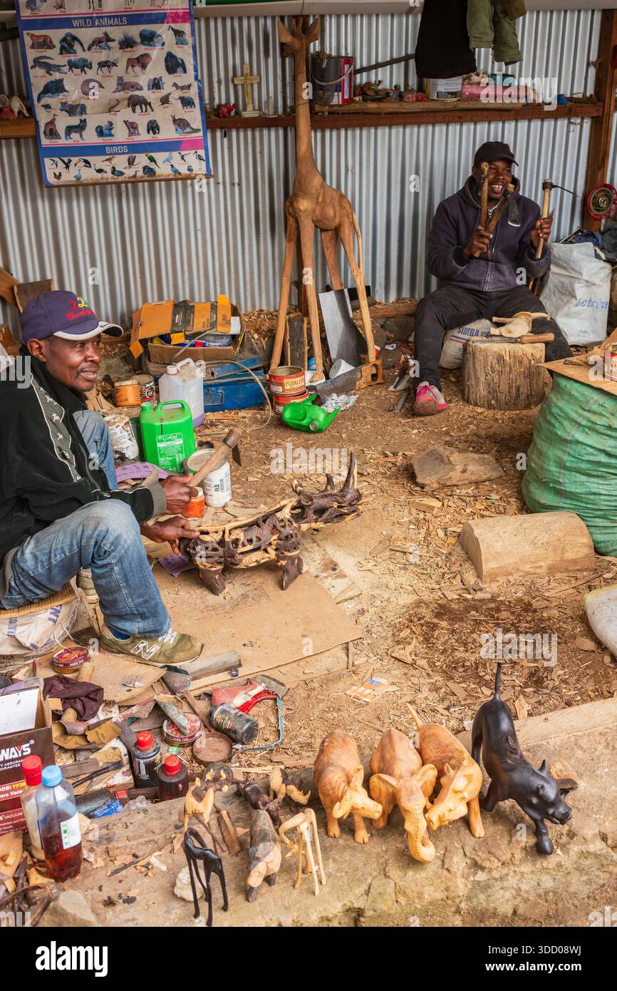 Migori, Kenya, - 17 giugno 2025: Vita cittadina vista dalla strada sterrata delle persone che lavorano e vivono. Gli artigiani creano sculture in legno di animali da vendere Foto Stock