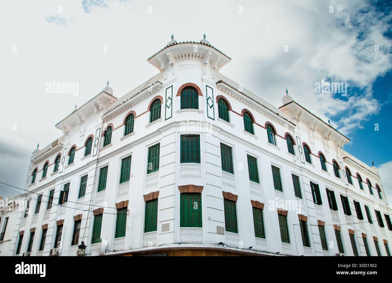 Storico edificio bianco a Tetouan in stile ispano-moresco, persiane verdi, archi decorativi e una facciata elegante sotto un cielo parzialmente nuvoloso. Foto Stock