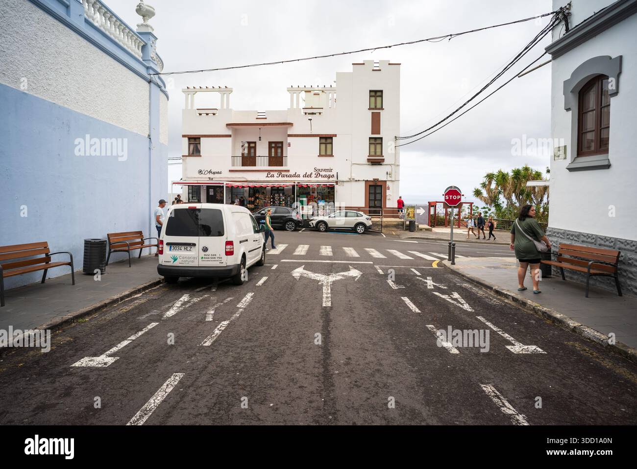 ICOD DE LOS VINOS, SPAGNA - 2 AGOSTO 2025: Strada con auto parcheggiate e pedoni vicino all'edificio del negozio di souvenir e alla passerella. Tenerife, Isole Canarie Foto Stock