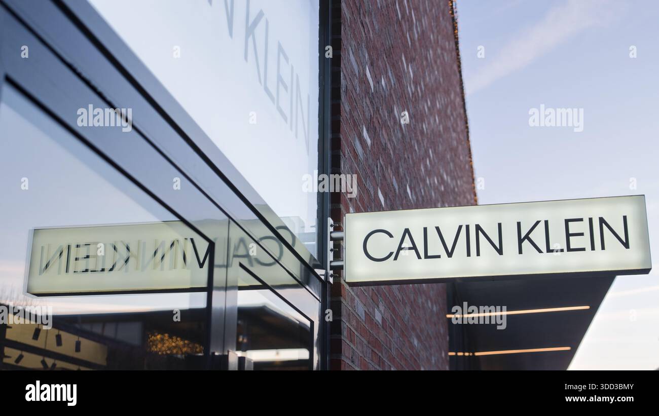 Insegna di moda illuminata montata su un edificio con finestre in vetro riflettente, che si illuminano con una calda luce del tramonto. Outletcity Metzingen Foto Stock