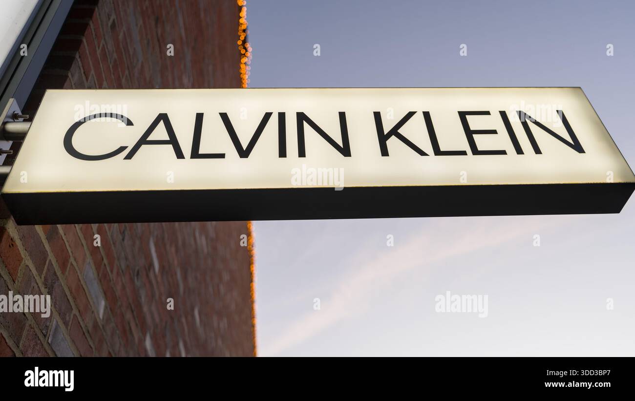 Un marchio di moda illuminato, montato su una parete di mattoni sotto un cielo sereno, crea un'atmosfera urbana pulita e moderna. Outletcity Metzingen Foto Stock