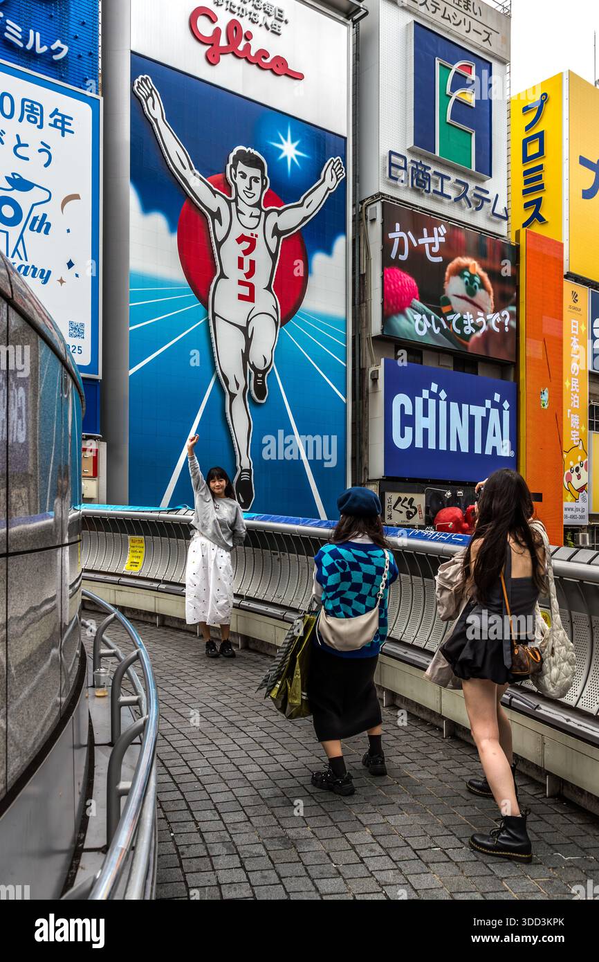 Tre donne fotografano il cartellone Glico sul Canale Dotonbori di Osaka, Giappone. Il famoso Glico Man originariamente pubblicizzava un Energy bar contenente ingredienti di ostriche. Osaka, Prefettura di Osaka, Giappone Foto Stock