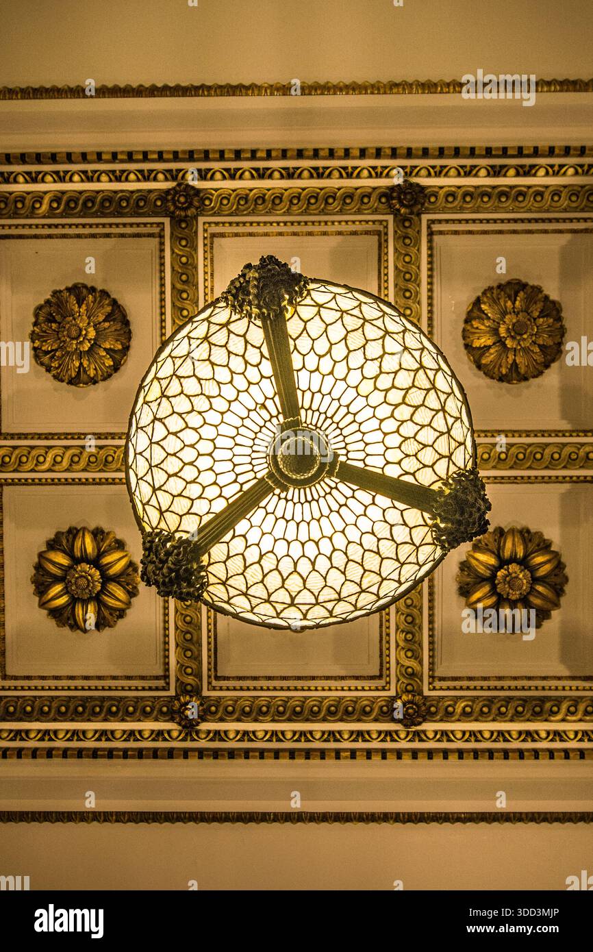 Vista diretta verso l’alto di un apparecchio da soffitto in vetro antico stile Tiffany circondato da rosoni in gesso a cassettoni decorati a Chicago. Foto Stock