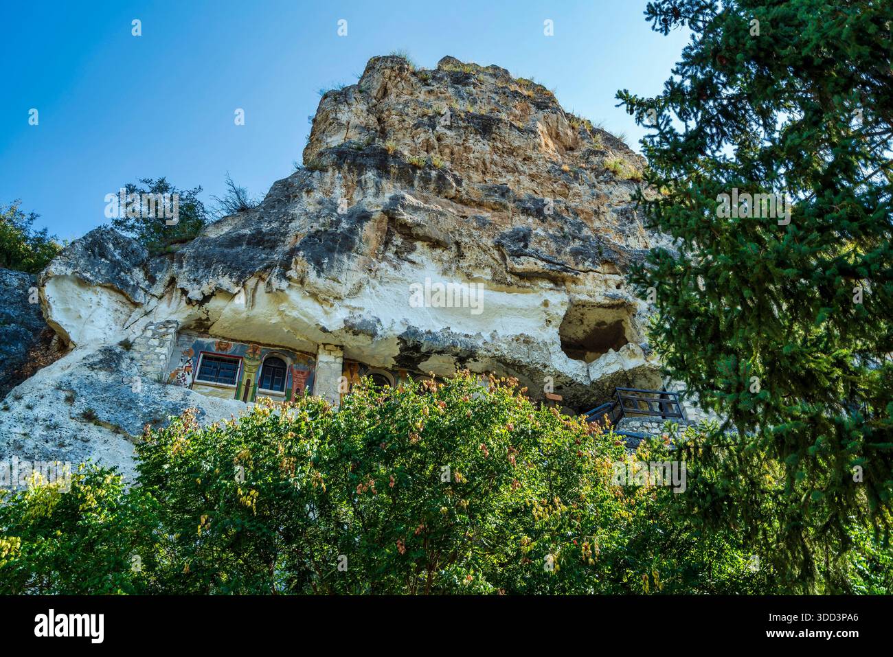 Monastero ortodosso scavato nella scogliera calcarea vicino a Ruse, Bulgaria, circondato dal verde e dal cielo blu, con affreschi religiosi. Foto Stock