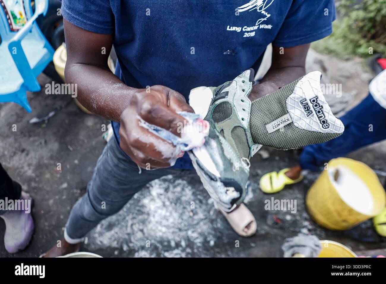 Un commerciante di scarpe di seconda mano che pulisce le scarpe al mercato Gikomba. I commercianti Jua Kali di Nairobi (le parole sono una traduzione diretta di "sole caldo" in swahili) sono una forza resiliente nell'economia informale del Kenya, radicata nell'autosufficienza, nella produzione di prodotti metallici, nel riciclaggio, nella riparazione di automobili, spingere carri, distributori automatici di acqua, gestire piccoli negozi, vendere diversi tipi di merci sul mercato, tra molti altri commerci in condizioni difficili, diventando un centro vivace per artigiani e uomini d'affari che creano e vendono tutto, affrontando sfide come frequenti incendi, sfratti e lacune politiche, ma anche Foto Stock