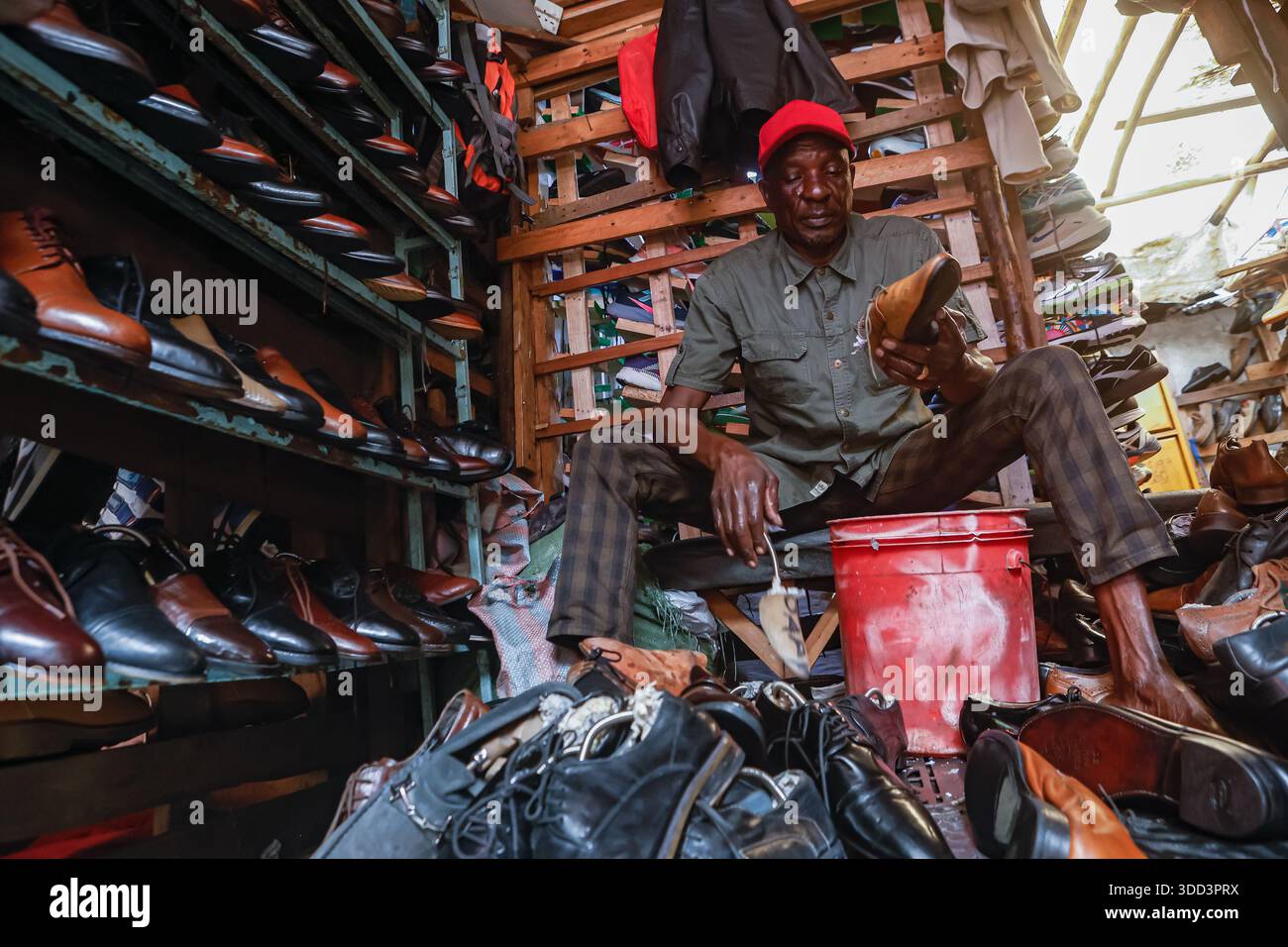 Un commerciante di scarpe di seconda mano che pulisce le scarpe al mercato Gikomba. I commercianti Jua Kali di Nairobi (le parole sono una traduzione diretta di "sole caldo" in swahili) sono una forza resiliente nell'economia informale del Kenya, radicata nell'autosufficienza, nella produzione di prodotti metallici, nel riciclaggio, nella riparazione di automobili, spingere carri, distributori automatici di acqua, gestire piccoli negozi, vendere diversi tipi di merci sul mercato, tra molti altri commerci in condizioni difficili, diventando un centro vivace per artigiani e uomini d'affari che creano e vendono tutto, affrontando sfide come frequenti incendi, sfratti e lacune politiche, ma anche Foto Stock