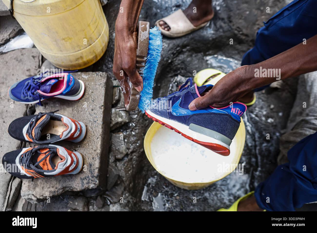 Un commerciante di scarpe di seconda mano che pulisce le scarpe al mercato Gikomba. I commercianti Jua Kali di Nairobi (le parole sono una traduzione diretta di "sole caldo" in swahili) sono una forza resiliente nell'economia informale del Kenya, radicata nell'autosufficienza, nella produzione di prodotti metallici, nel riciclaggio, nella riparazione di automobili, spingere carri, distributori automatici di acqua, gestire piccoli negozi, vendere diversi tipi di merci sul mercato, tra molti altri commerci in condizioni difficili, diventando un centro vivace per artigiani e uomini d'affari che creano e vendono tutto, affrontando sfide come frequenti incendi, sfratti e lacune politiche, ma anche Foto Stock