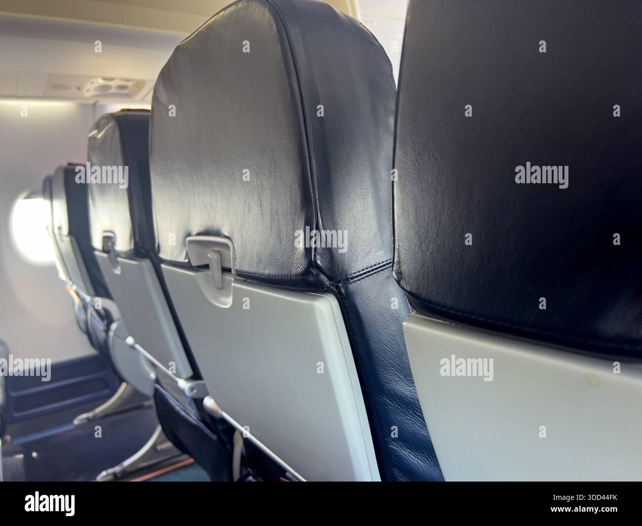 Sedili aerei vuoti con tavolini ripiegati e luce finestrino che entra in cabina Foto Stock