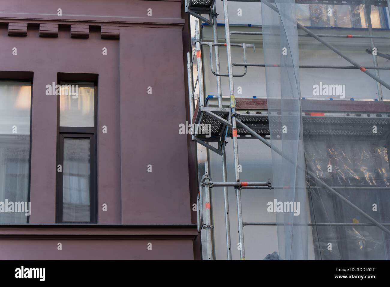 Facciata ristrutturata di edifici con ponteggi in metallo, rete di sicurezza protettiva, dettagli di finestre e pareti esterne durante i lavori di costruzione urbana Foto Stock
