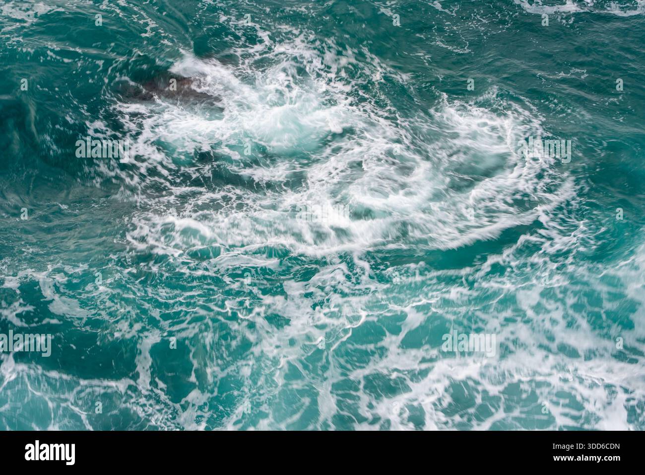 L'acqua dell'oceano scorre con una schiuma bianca vorticosa e toni verdi profondi. Foto Stock