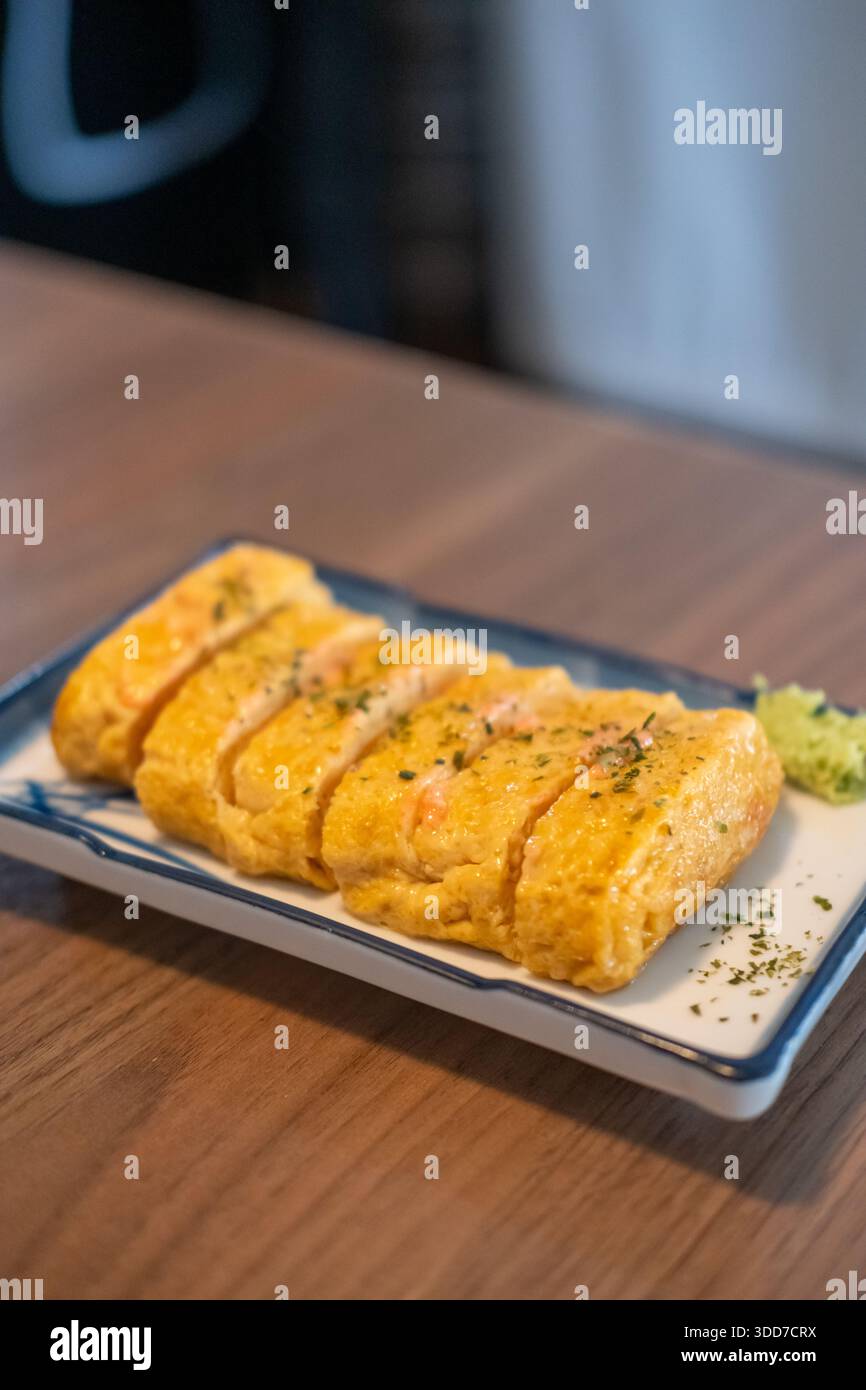 Tamagoyaki, un'omelette giapponese preparata arrotolando diversi strati di uova sbattute fritte, servita su un piatto. Foto Stock