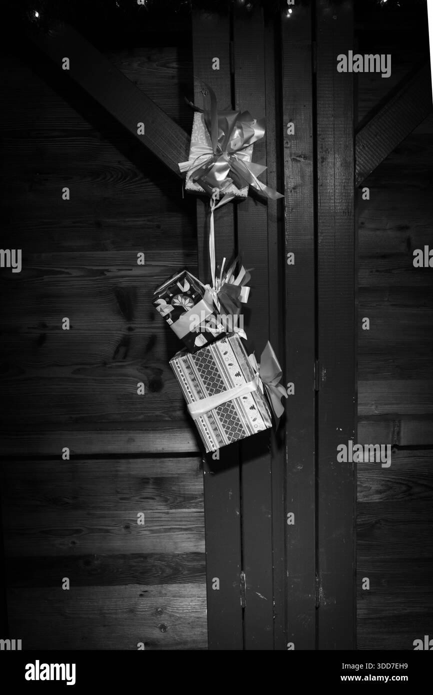 Fotografia in bianco e nero di regali di Natale avvolti appesi, utilizzati come decorazioni festive su una parete rustica in legno. La confezione regalo disposta verticalmente Foto Stock