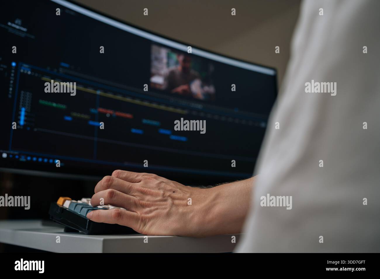 Editor che lavora su un software di editing video professionale, utilizzando una workstation con ampio monitor che mostra la timeline e i video clip codificati a colori Foto Stock