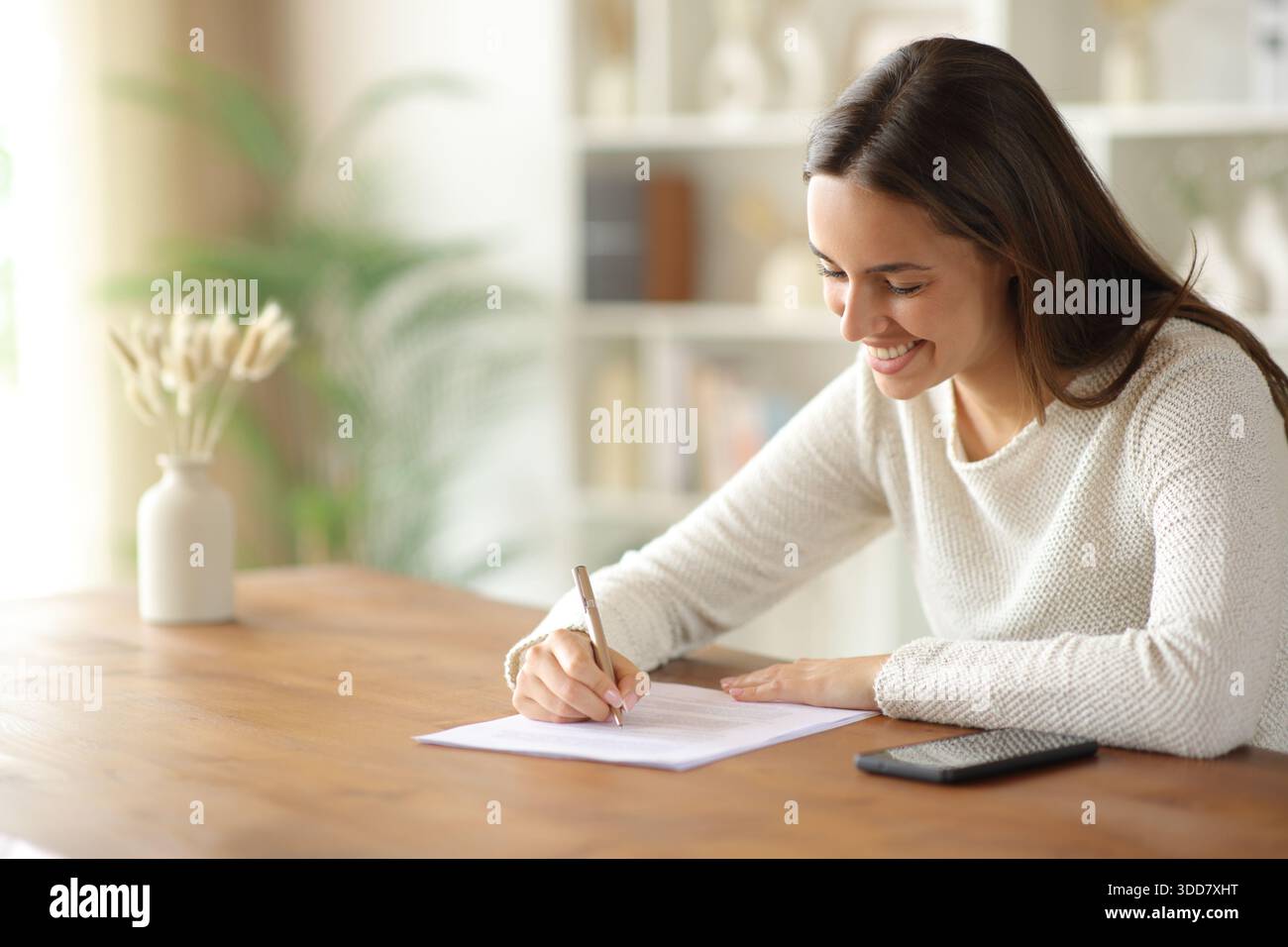 Donna felice che compila il modulo su un tavolo di legno a casa Foto Stock