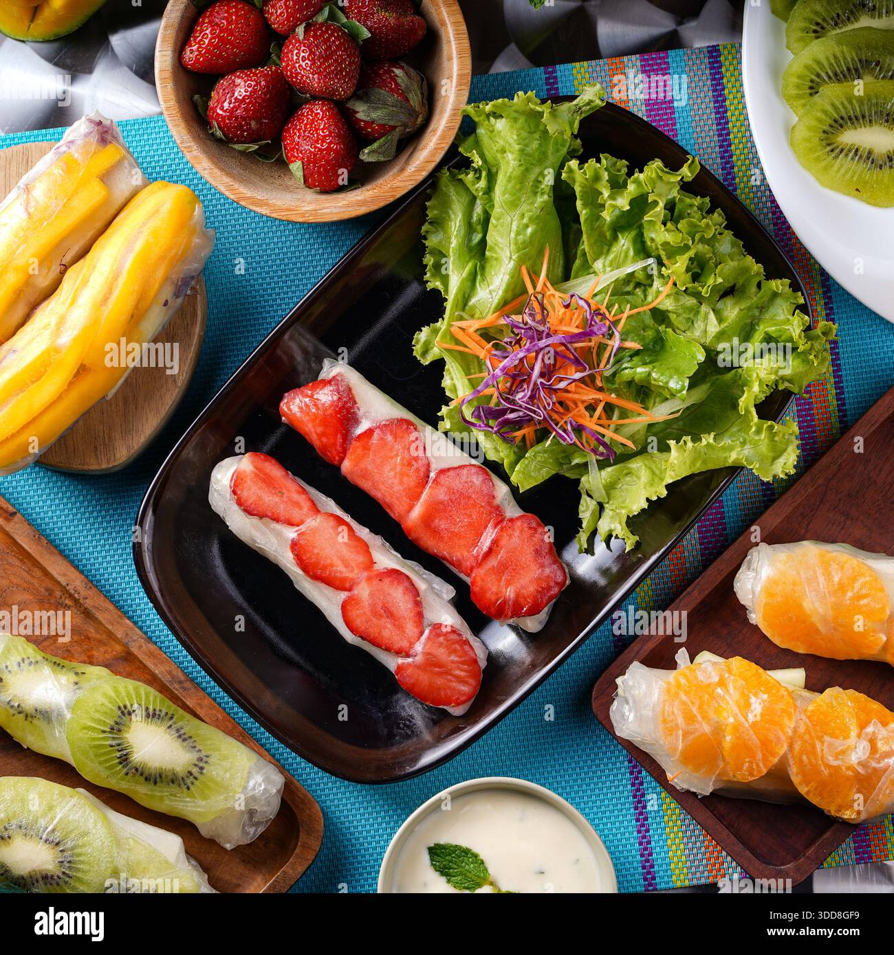 Sushi di frutta assortita, verdure fresche e salsa serviti su una tovaglia vibrante, perfetto per uno spuntino o un dessert salutare. Foto Stock