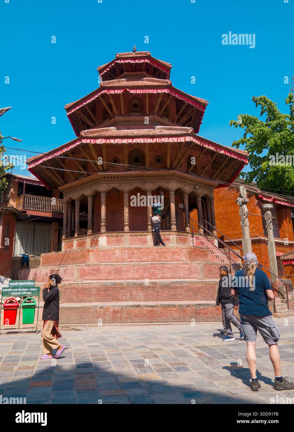 Tradizionale tempio nepalese con tetti a più livelli e visitatori che camminano intorno, mostrando l'architettura storica e il patrimonio culturale in una vivace atmosfera Foto Stock