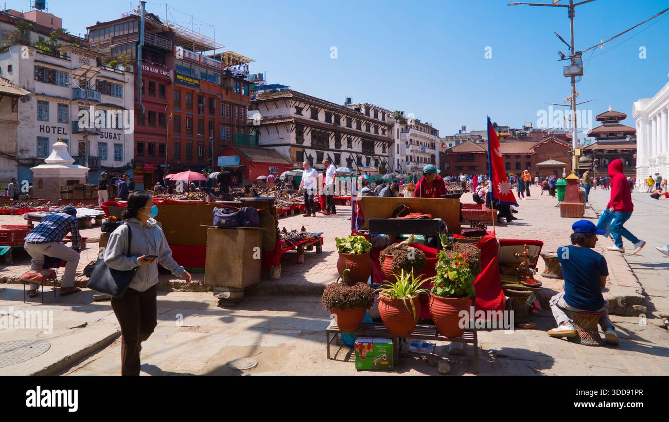 Vivace piazza del mercato con gente e vegetazione sotto un cielo blu luminoso. Foto Stock