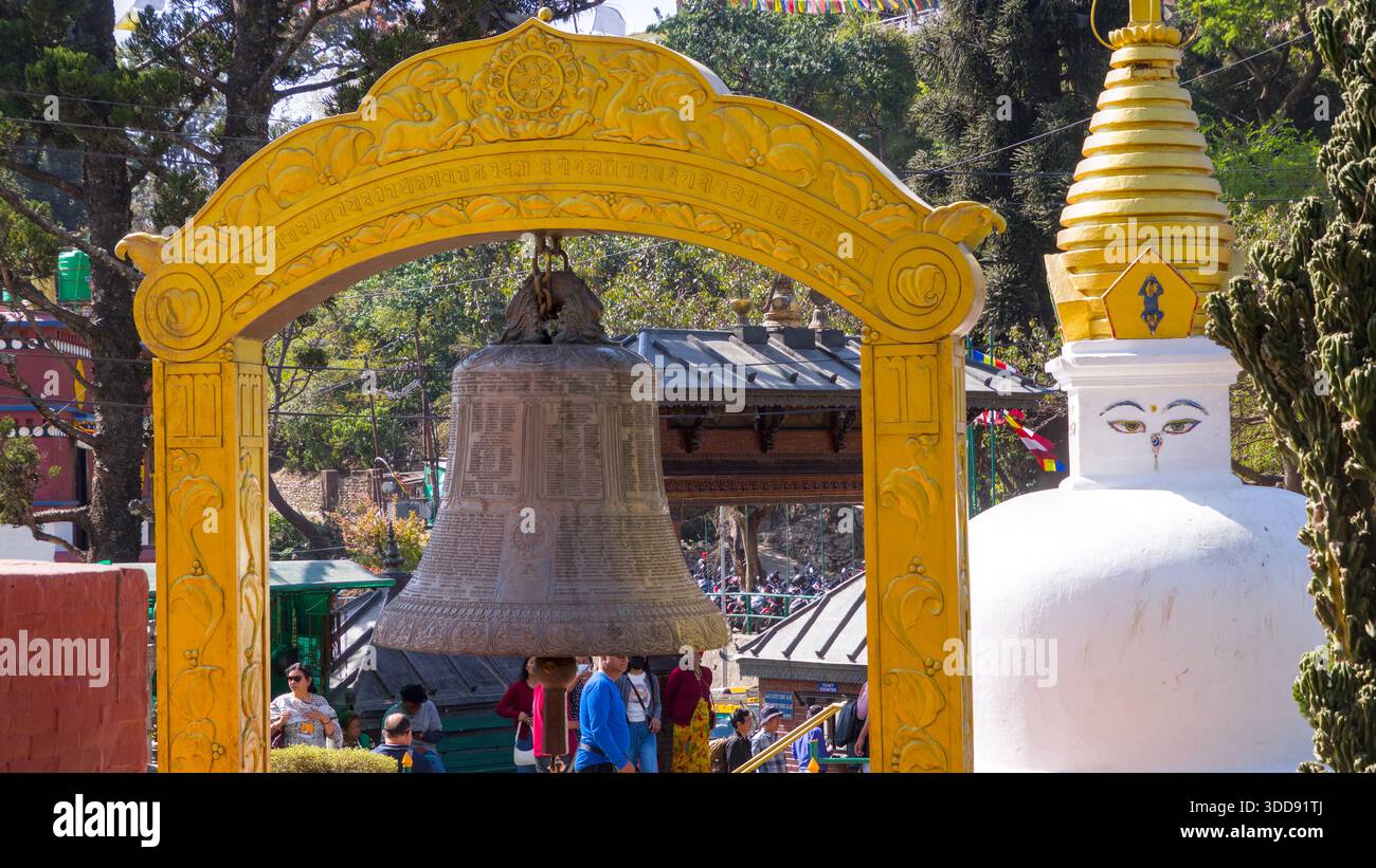 Campanile giallo che incornicia una grande campana con un vicino stupa in un ambiente soleggiato e vivace. Foto Stock