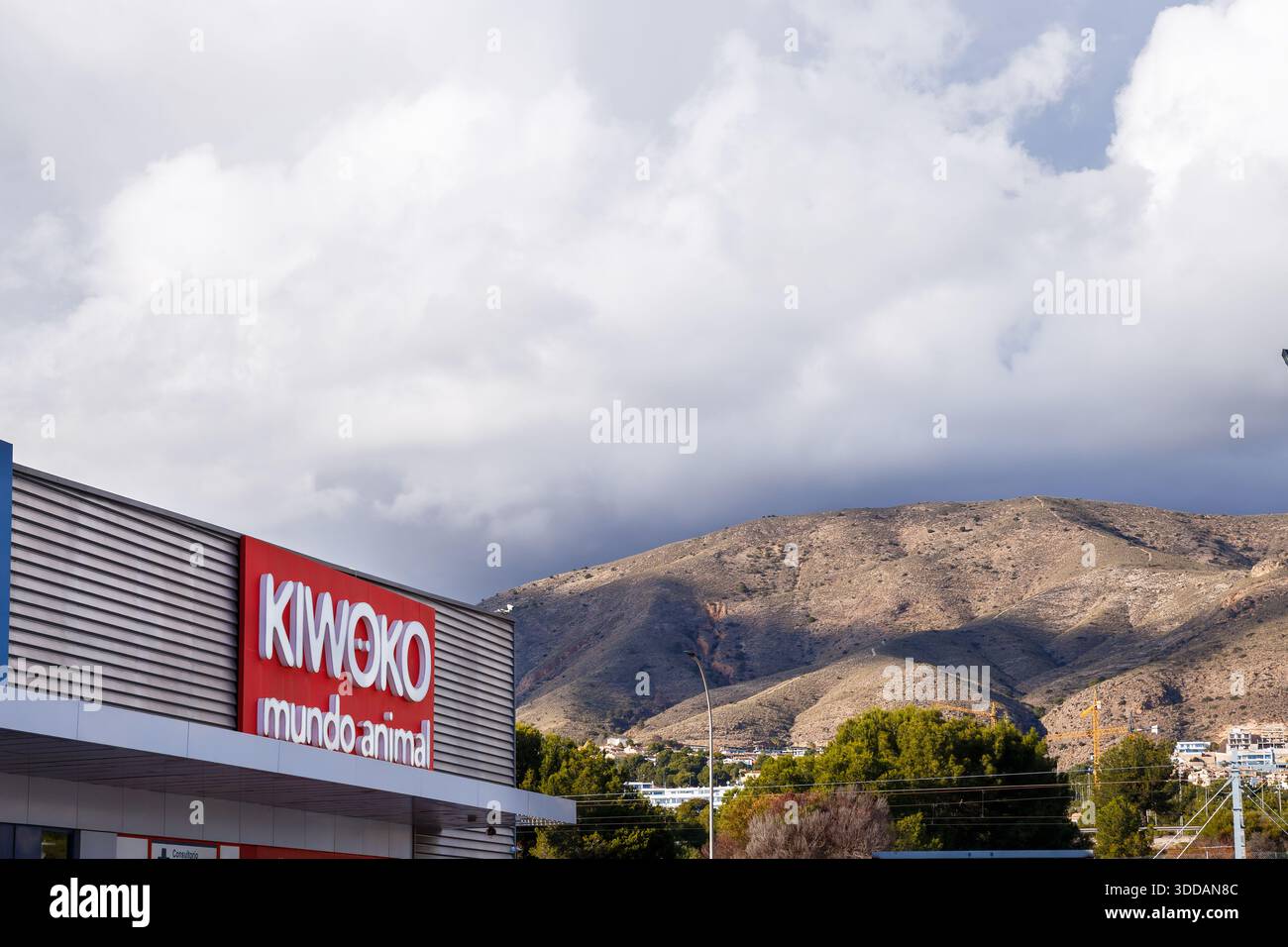 L'esterno di un negozio Kiwoko 'Mundo Animal' a Finestrat, incorniciato contro le aspre montagne di Puig Campana e un cielo nuvoloso. Foto Stock