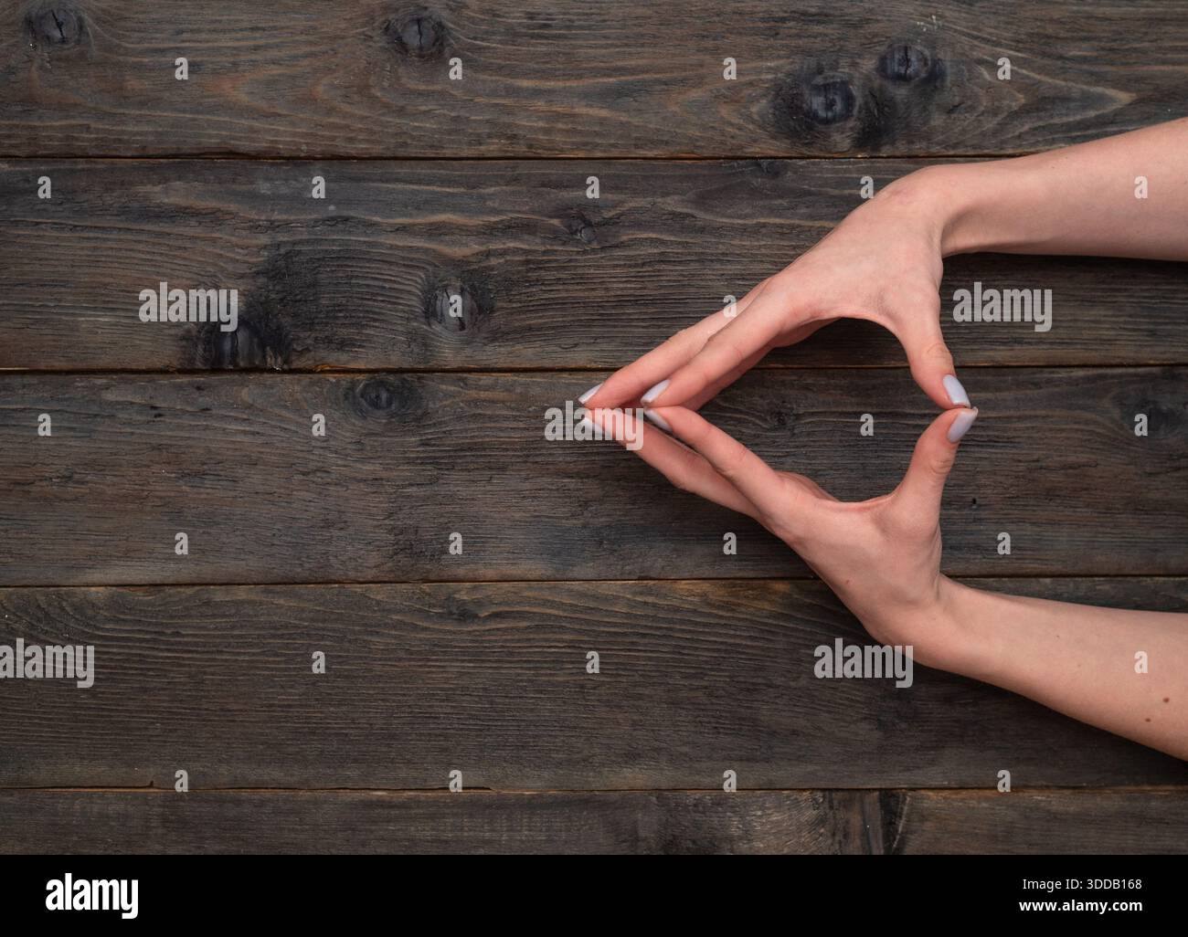 Due mani modellano una figura triangolare con le dita posizionate con cura su sfondo in legno. l'immagine trasmette unità e creatività, perfetta per il desiderio astratto Foto Stock