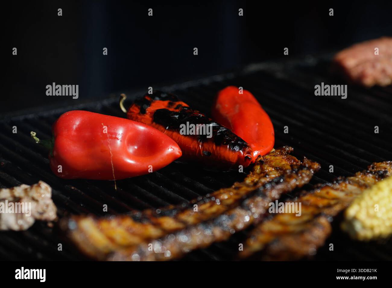 Mais, paprika rossa e costolette di maiale su griglia esterna in metallo antracite. Foto Stock