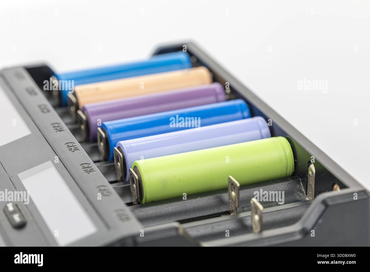 Primo piano di un caricabatterie nero con batterie multicolore. Le batterie sono blu, marrone chiaro, viola e verde e disposte in fila. Lo sfondo è bianco Foto Stock