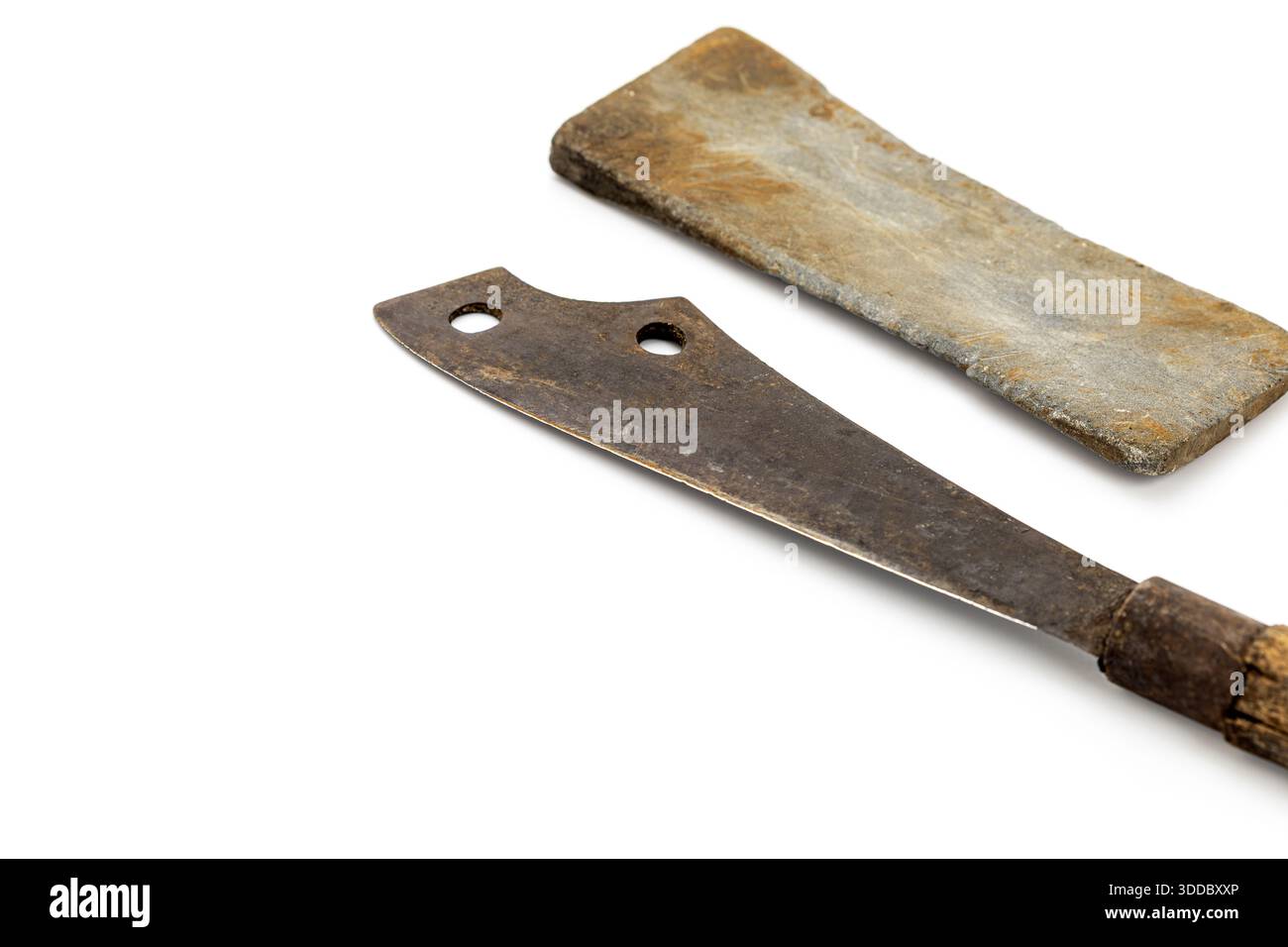 Sul bianco, accanto a una pietra affilatrice si trova un raschietto arrugginito vintage con manico in legno. Entrambi mostrano segni di età. La composizione è semplice, evidenziata Foto Stock