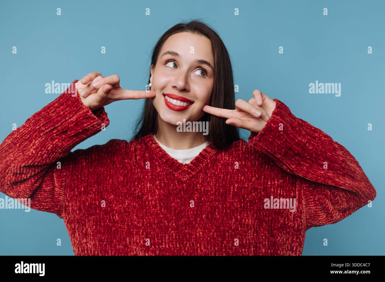 Donna in maglione rosso che sorride e punta le guance Foto Stock