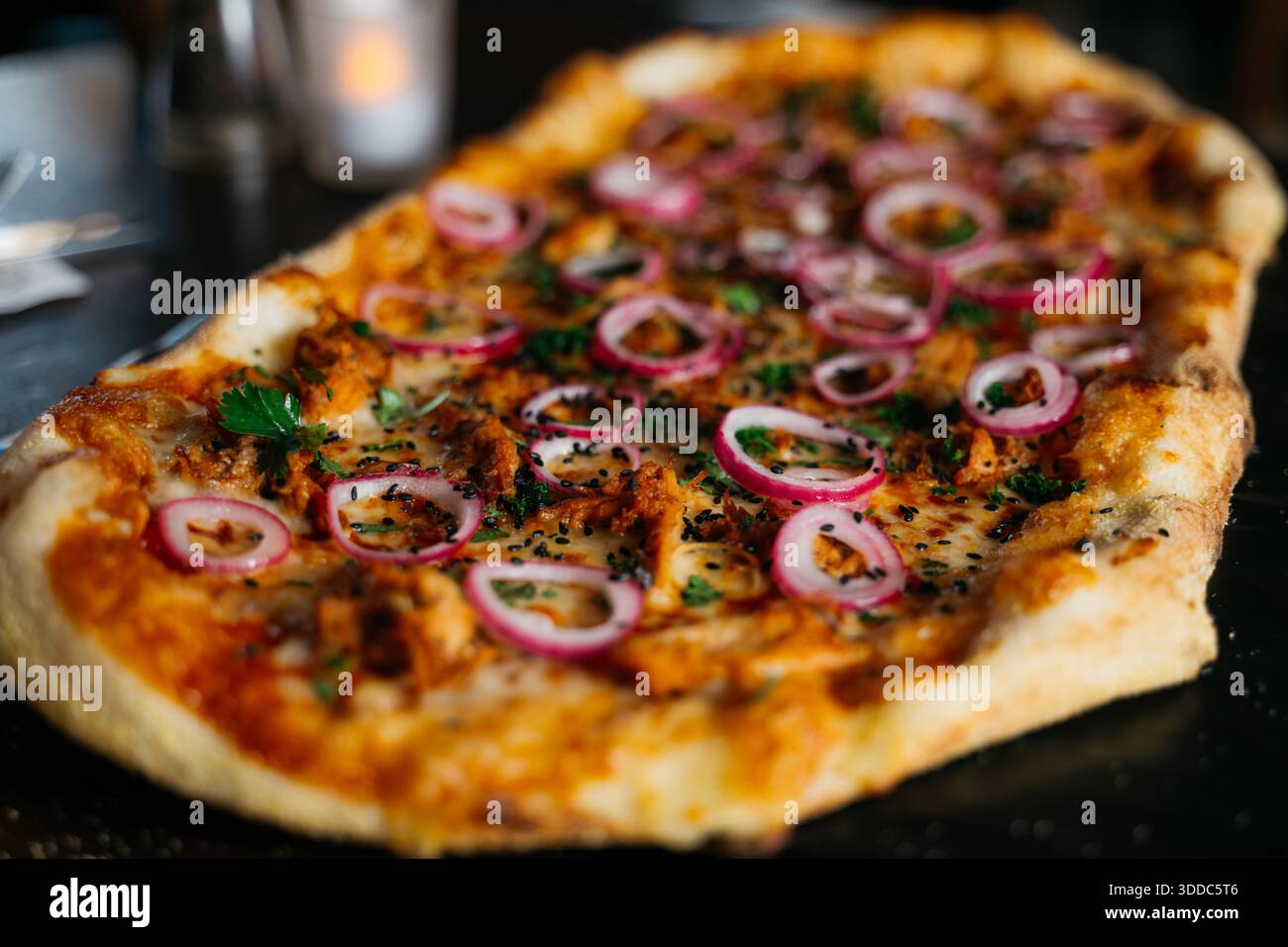 Una pizza grande con cipolle e condimenti di carne. La pizza è seduta su un tavolo. La pizza è molto grande e ha molti condimenti Foto Stock