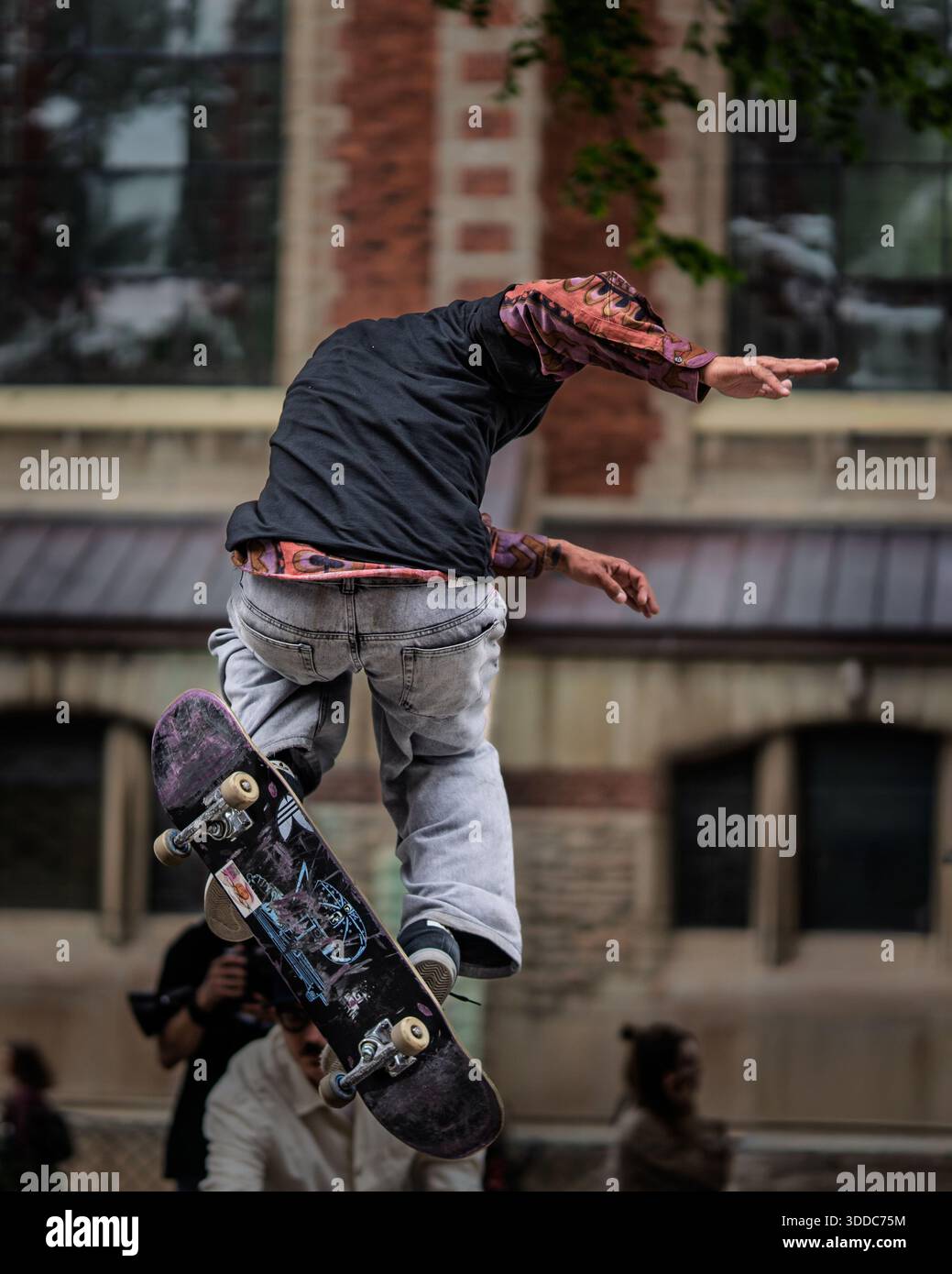Skateboarder che esegue un trucco su una barriera metallica in un ambiente urbano, con architettura storica in mattoni sfocata sullo sfondo. Foto Stock