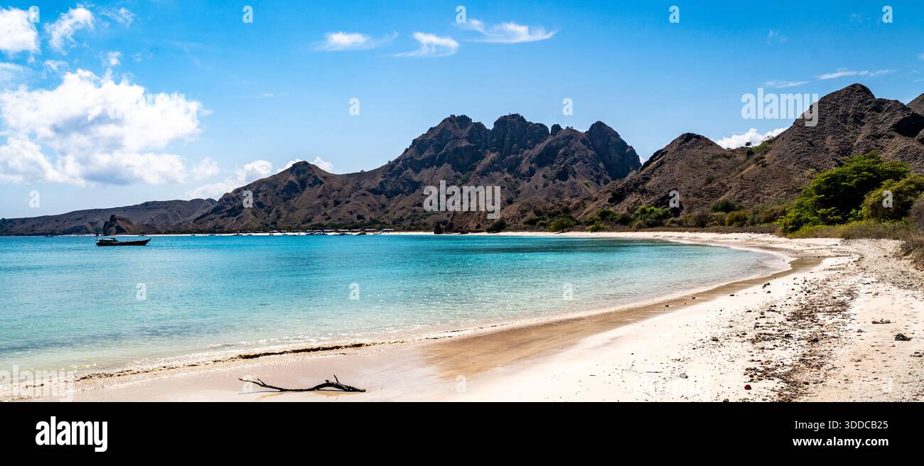 Spiaggia tropicale con acque turchesi, montagne e una barca. Foto Stock