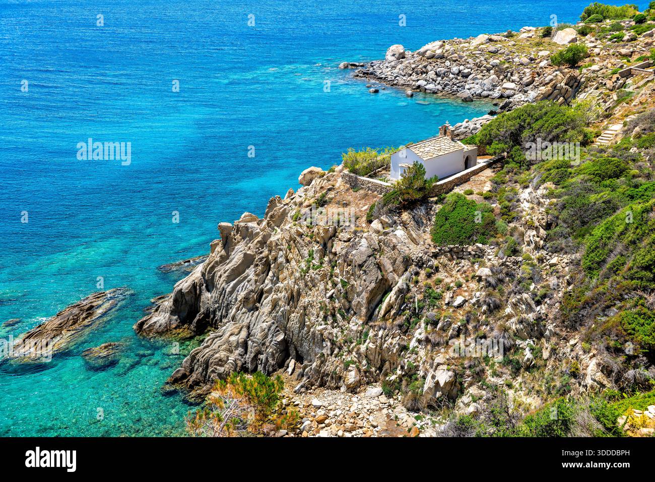Piccola chiesa greco-ortodossa a Karkinagri dell'isola di Ikaria, antico edificio greco lungo la scogliera della costa di montagna del mare di Icaria acque turchesi e cristalline Foto Stock