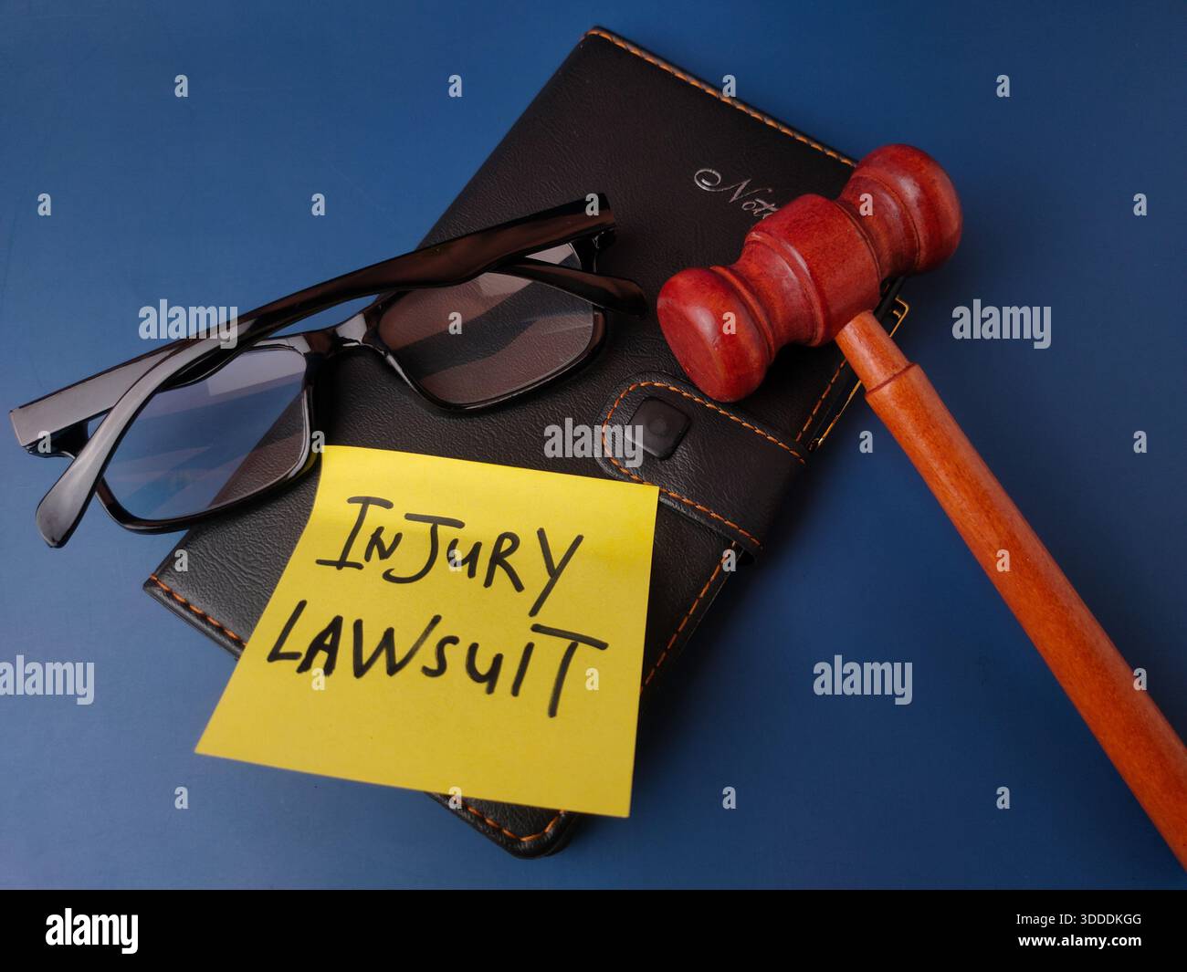 L'immagine mostra un concetto legale rappresentato da un martelletto, occhiali, notebook e una nota adesiva con il testo CAUSA PER INFORTUNIO. Foto Stock