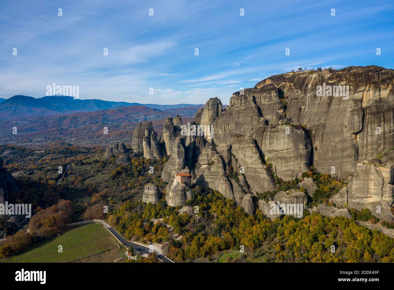 Il Monastero di Varlaam è arroccato su una spettacolare colonna di arenaria circondata da foreste autunnali e aspre montagne a Meteora, in Grecia. La scena presenta ampie formazioni rocciose sotto un cielo azzurro vivace, che creano un senso di grandezza e isolamento. Foto Stock