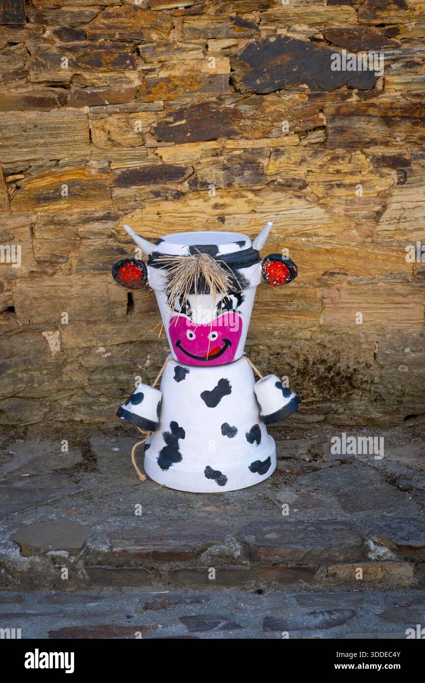 Stravagante figura di mucca fatta a mano realizzata in vasi di terracotta dipinti con capelli di paglia, in piedi contro un muro di pietra rustica, verticale Foto Stock