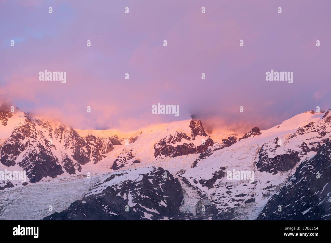 Il caldo rosa e arancione alpenglow illumina le cime innevate e le aspre creste del Monte bianco del Tacul, con morbide nuvole che attraversano il suggestivo paesaggio alpino. Foto Stock