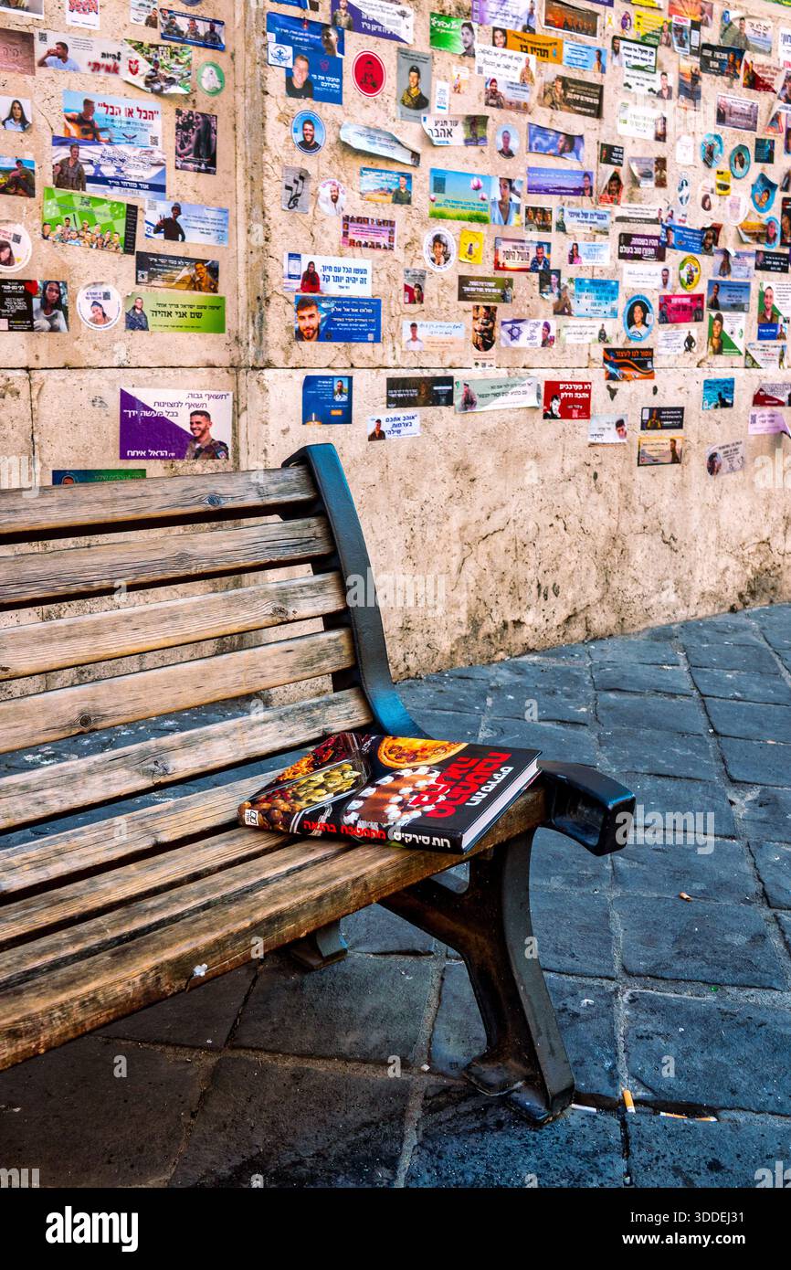 Libro di cucina ebraico su una panchina di fronte a un muro di adesivi commemorativi nel ghetto ebraico di Roma, Italia. Foto Stock