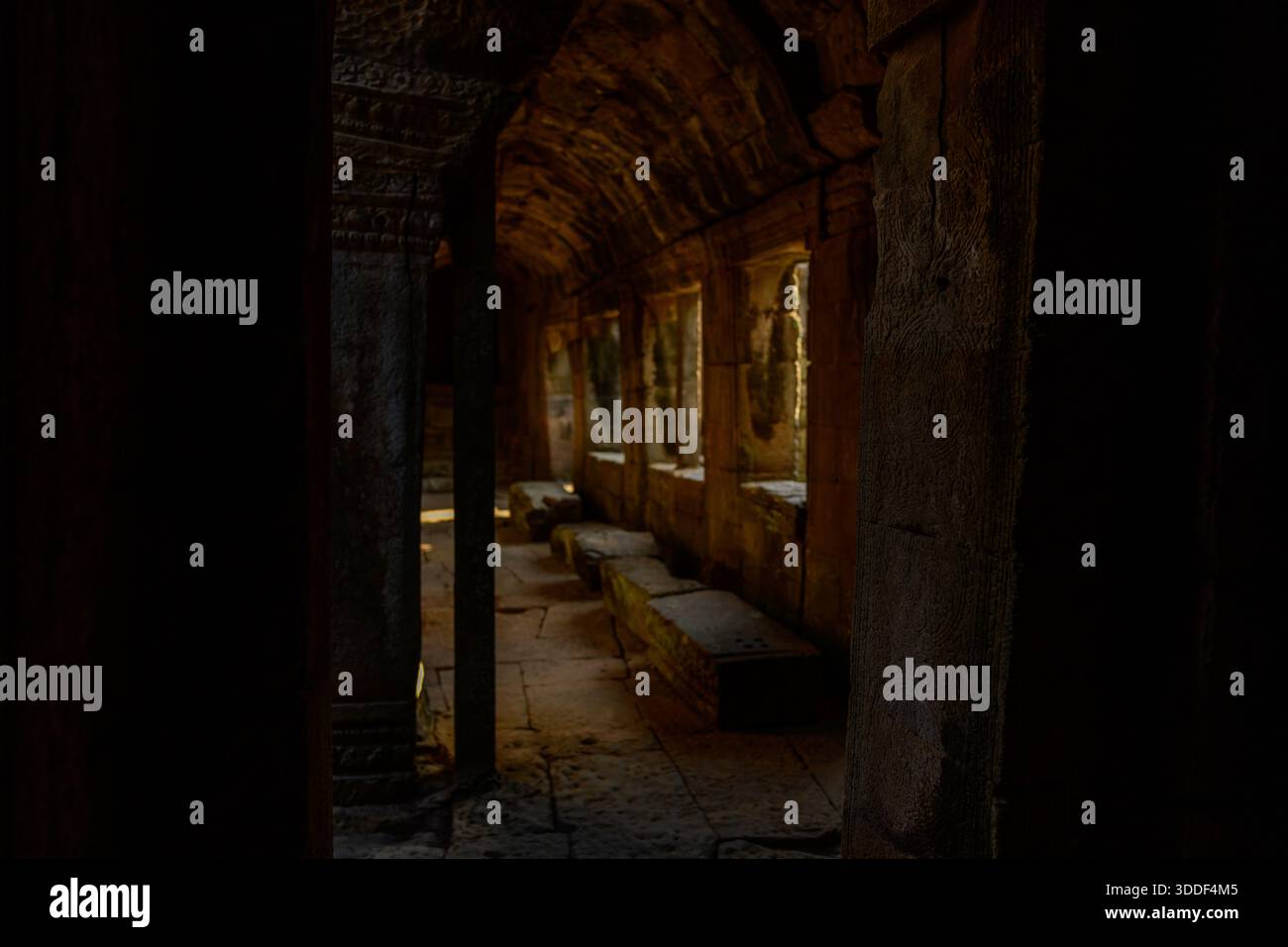 La luce naturale soffusa filtra attraverso le finestre in pietra, illuminando le pareti e le panchine di uno stretto corridoio all'interno del tempio Bayon ad Angkor, in Cambogia. L'arenaria intemprata e i dettagli scolpiti evocano un senso di mistero storico e di quiete isolamento. Foto Stock