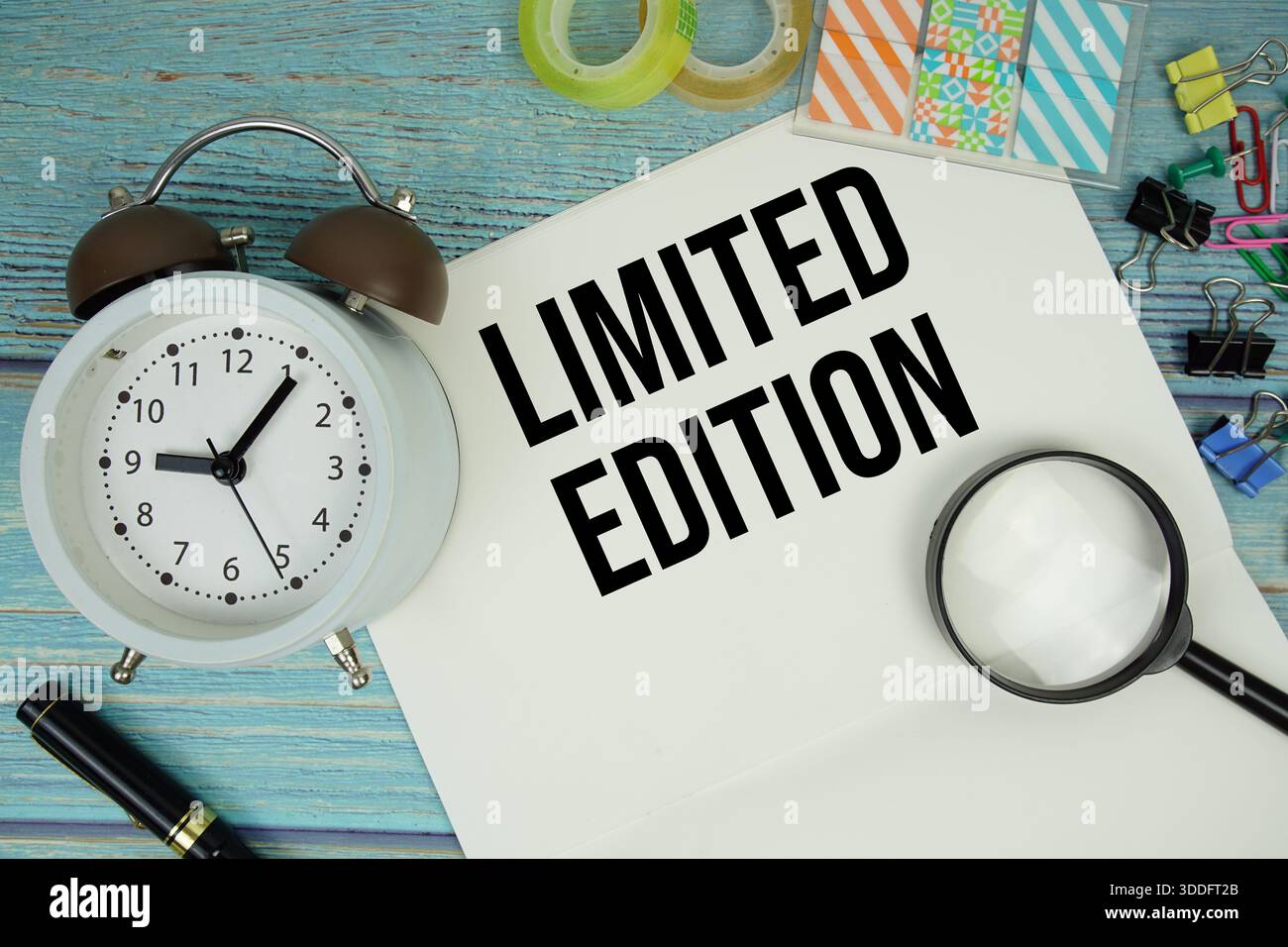 Testo in edizione limitata scritto su blocco note con sveglia e lente d'ingrandimento su fondo in legno Foto Stock
