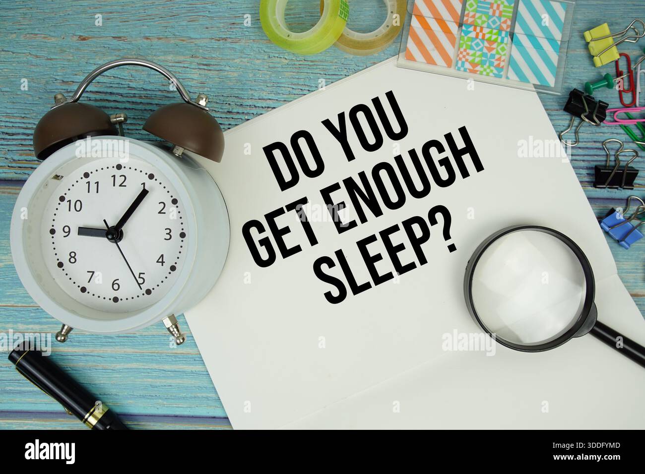 Hai abbastanza sonno? testo su un foglio circondato da forniture per ufficio, una lente d'ingrandimento e un orologio su una superficie di legno blu Foto Stock